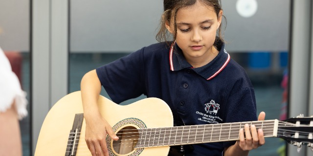 A girl playing guitar under instruction