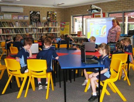 Students seated at tables in the school library during a guided learning session, highlighting collaborative learning, digital engagement and teacher support