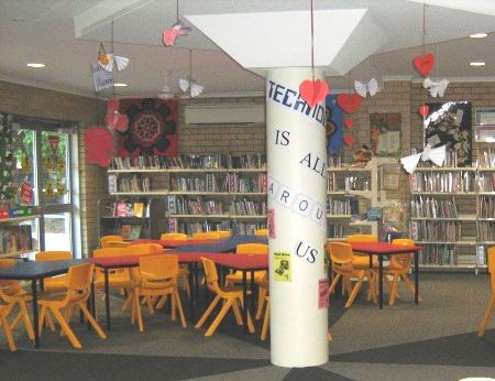School library with bookshelves and seating, displaying a message about teachers supporting learning, highlighting literacy, shared spaces and a welcoming learning environment